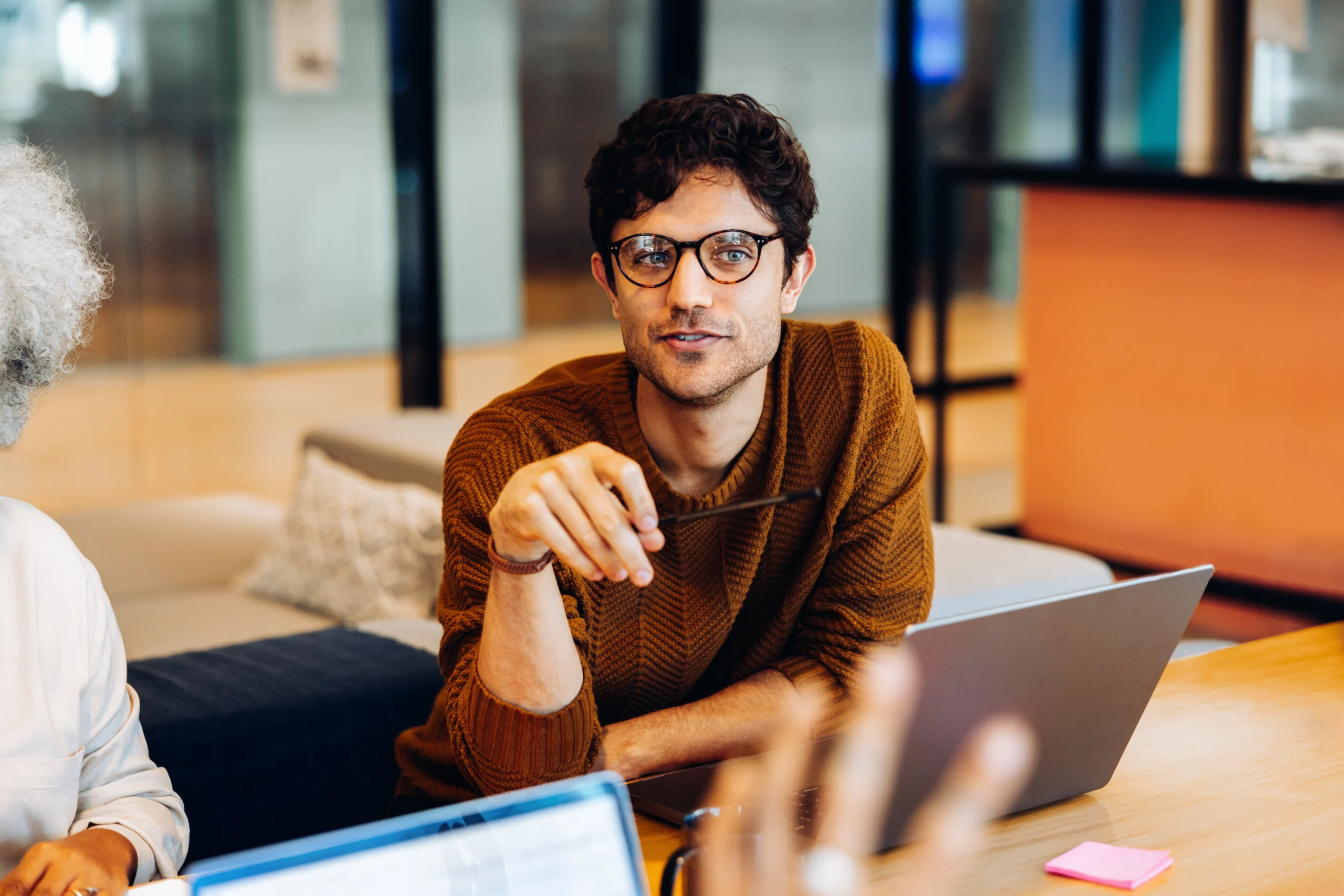 In the flow: Teammate sharing insight during the meeting A man with glasses sitting at a table and conversing with colleagues in an office environment.