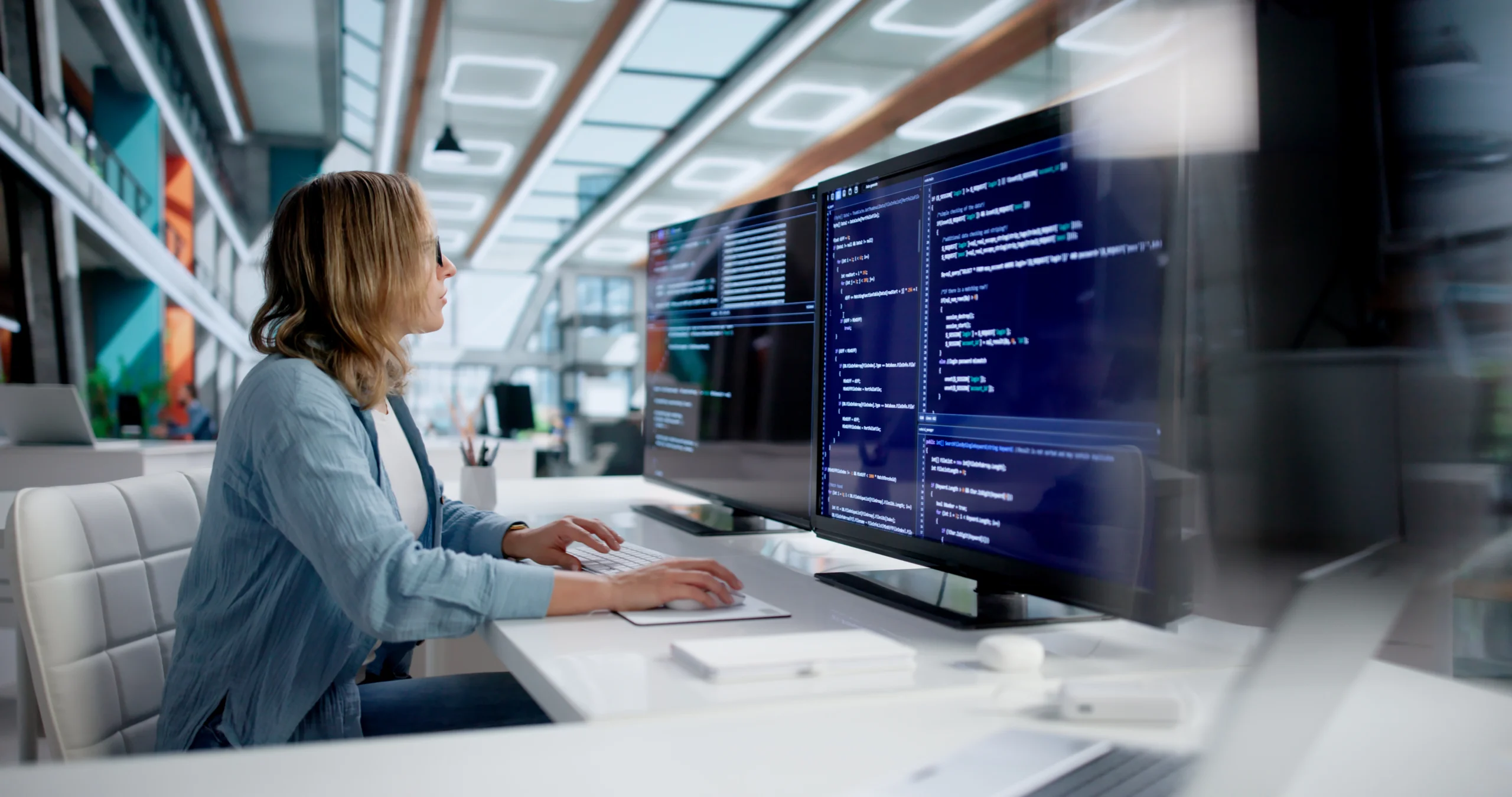 Skilled Female Software Developer A female software developer works at a desk within a brightly lit office space.